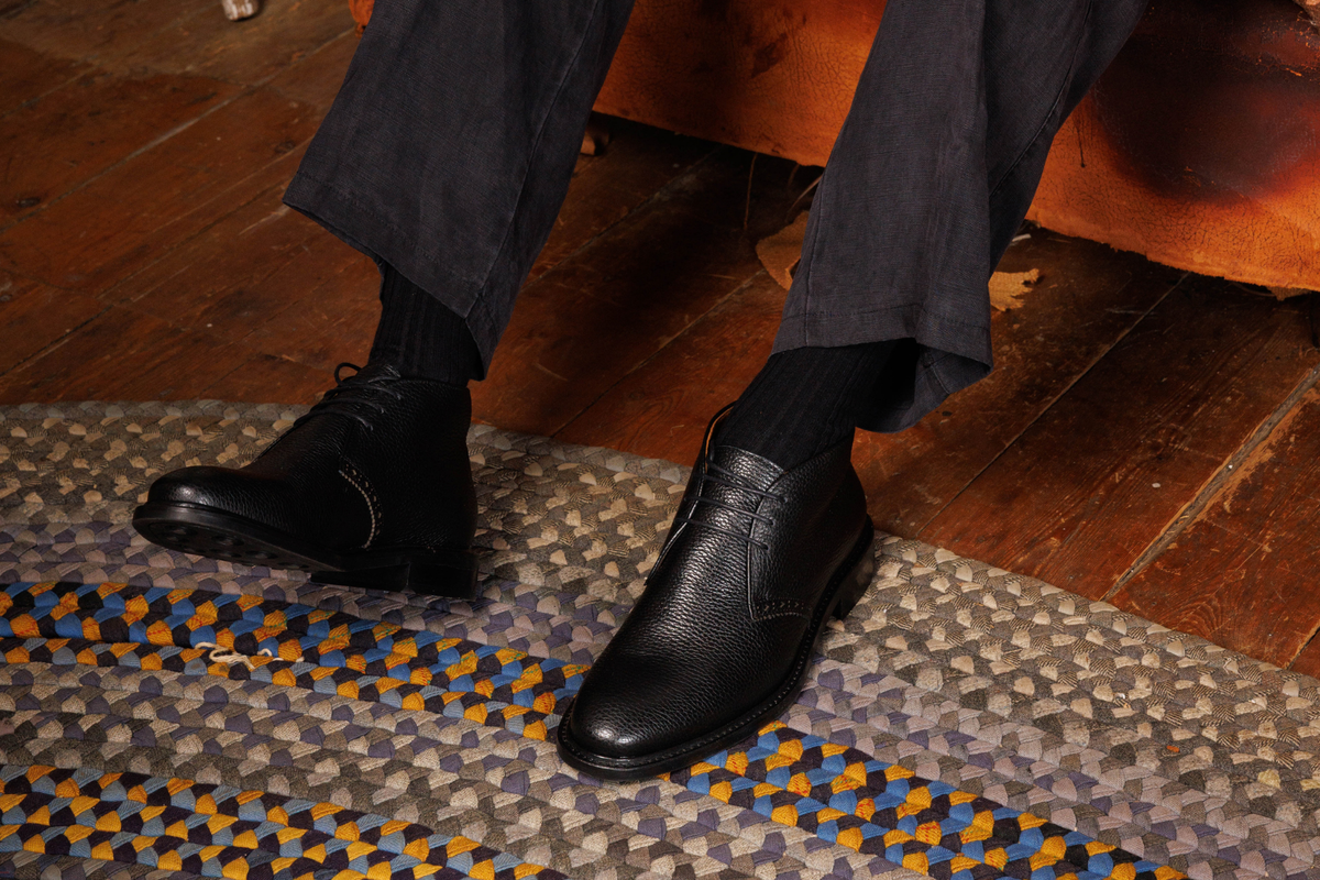 Wildsmith Model 12 chukka boots in Black Grain, worn with black socks and charcoal trousers on a braided rug